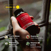Hand holding a bottle of Lion's Mane Mushroom supplement with product details on a blurred natural background