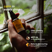 Hand holding a CBD spray bottle with product details on a blurred natural background